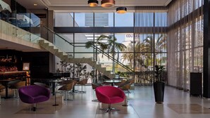 A spacious lobby with modern seating, a staircase, and large windows offering views of palm trees and a building. - Golden Tulip Sao Jose Dos Campos (São José dos Campos)