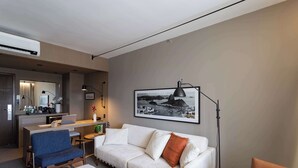 A modern hotel room with a sofa, a desk, a chair, a dining table, and a large framed picture on the wall. - Golden Tulip Sao Jose Dos Campos (São José dos Campos)