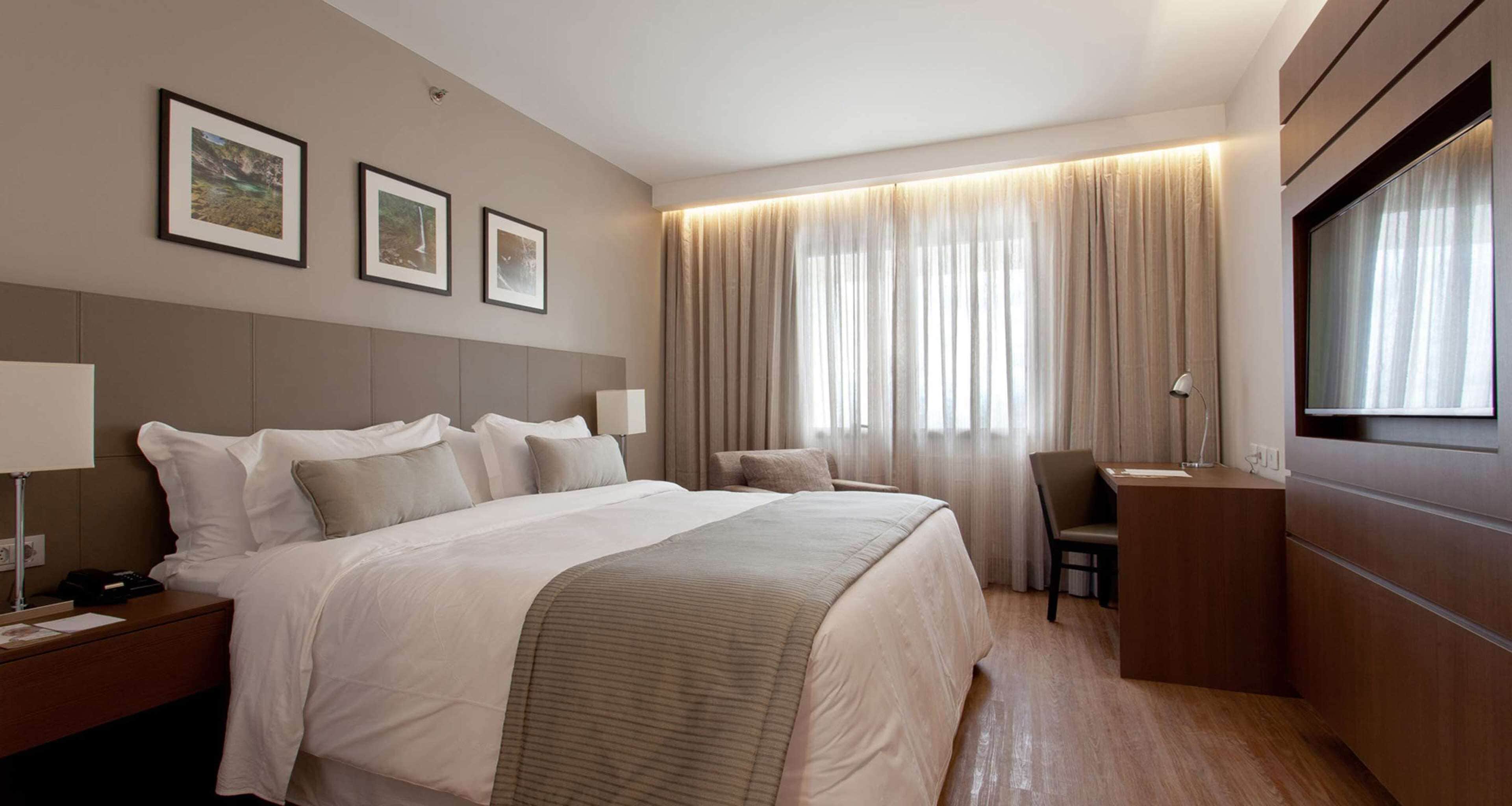 Habitación de hotel con una cama grande, un escritorio, una silla y un televisor. Hay tres cuadros enmarcados en la pared.