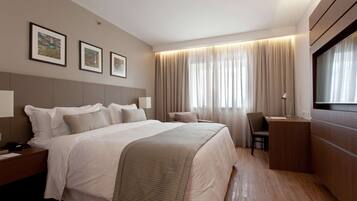 Habitación de hotel con una cama grande, un escritorio, una silla y un televisor. Hay tres cuadros enmarcados en la pared.