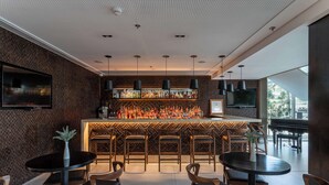 A modern bar area with a long counter, multiple bar stools, and a television screen. - Golden Tulip Sao Jose Dos Campos (São José dos Campos)