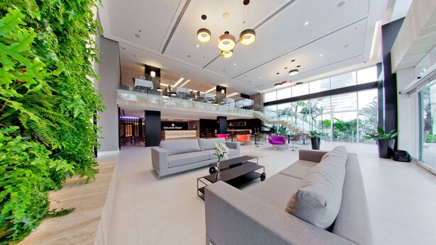 A spacious lobby with a modern design, featuring a grey sofa, a coffee table, and a reception desk. - Golden Tulip Sao Jose Dos Campos (São José dos Campos)
