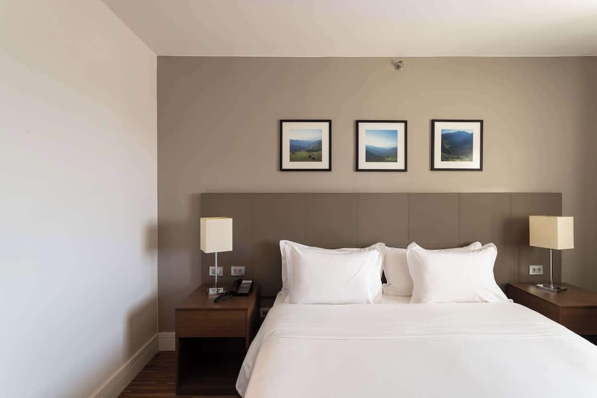 A hotel room with a large bed, two bedside tables with lamps, and three framed pictures on the wall.