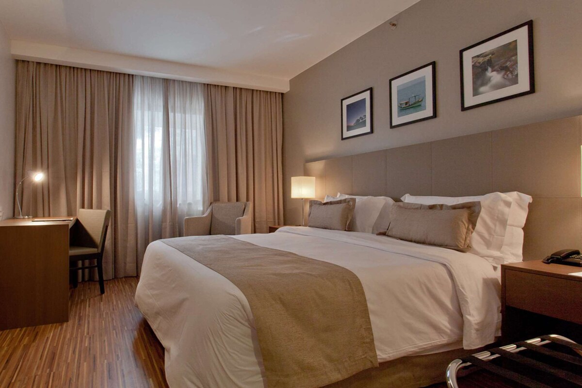 A hotel room with a large bed, a desk, and two chairs. There are curtains on the windows, and three framed pictures on the wall.