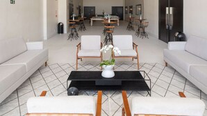 A spacious lobby with a modern design, featuring a central seating area with sofas and chairs, a dining area with tables and chairs, and a large black refrigerator. - Golden Tulip Sao Jose Dos Campos (São José dos Campos)