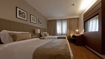 A hotel room with two beds, a desk, a chair, and a large window with curtains.
