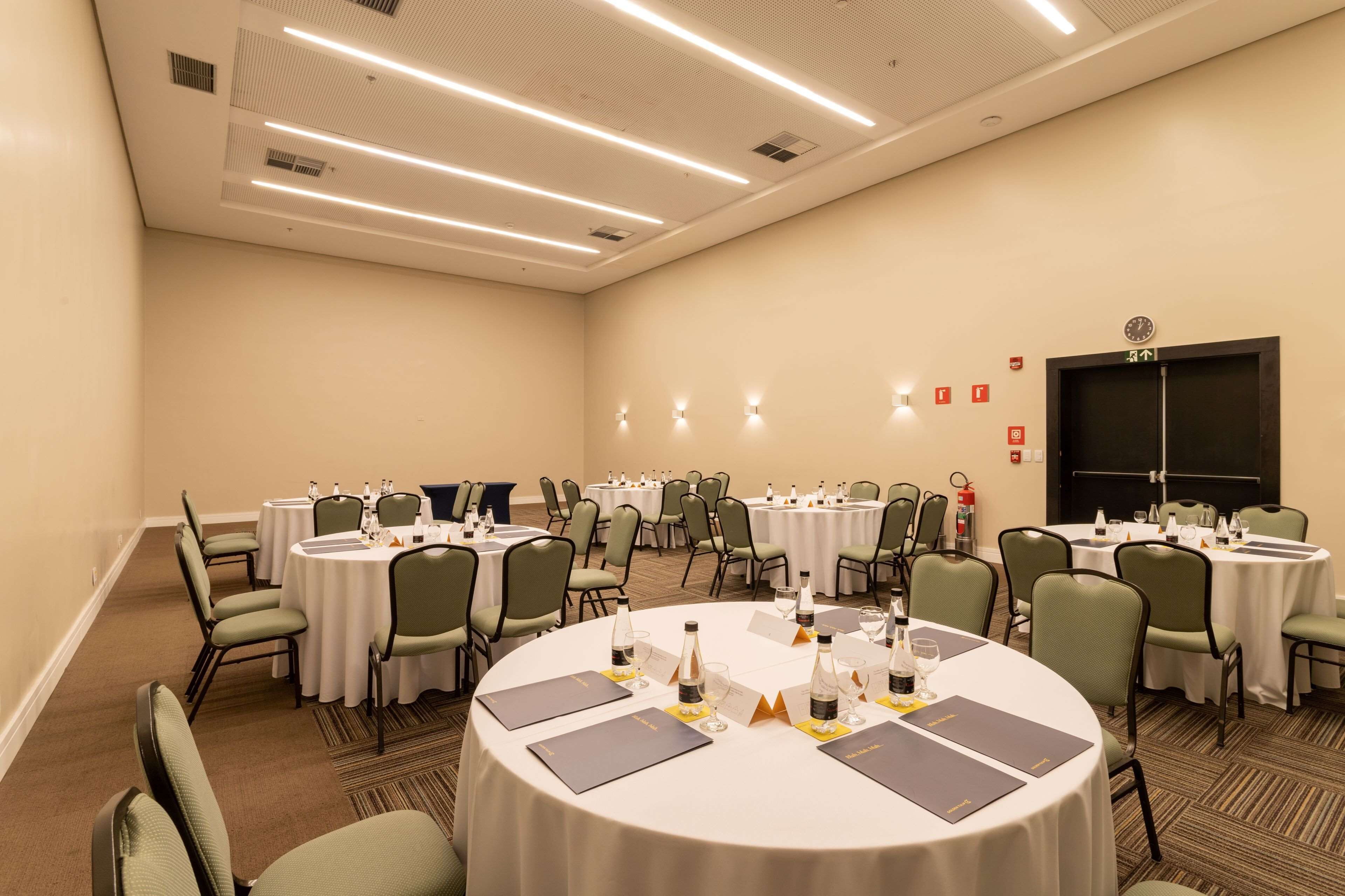A conference room with multiple round tables, each set with chairs, name cards, and water bottles.