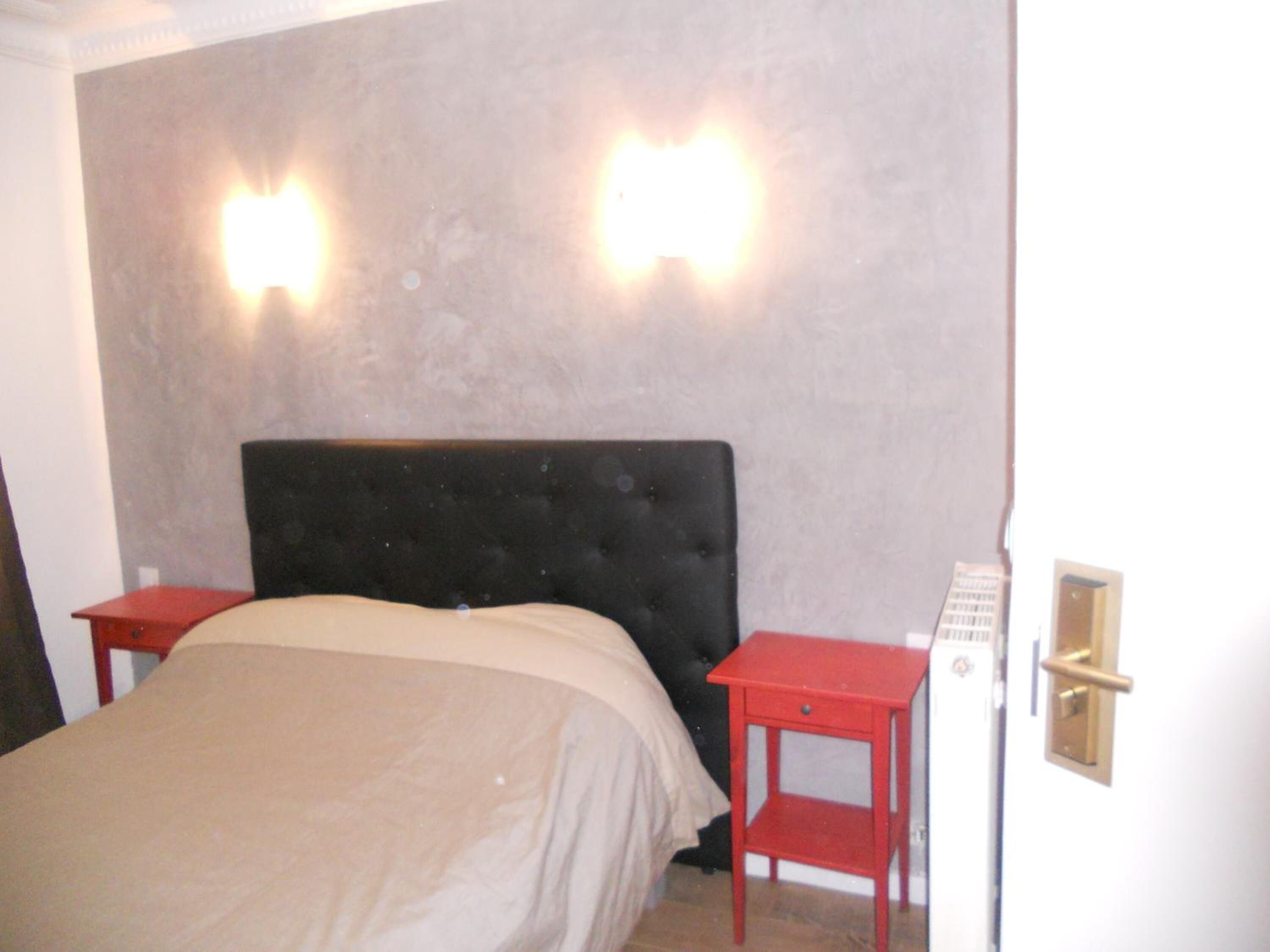 A bedroom with a bed, two nightstands, and a wall-mounted light fixture.
