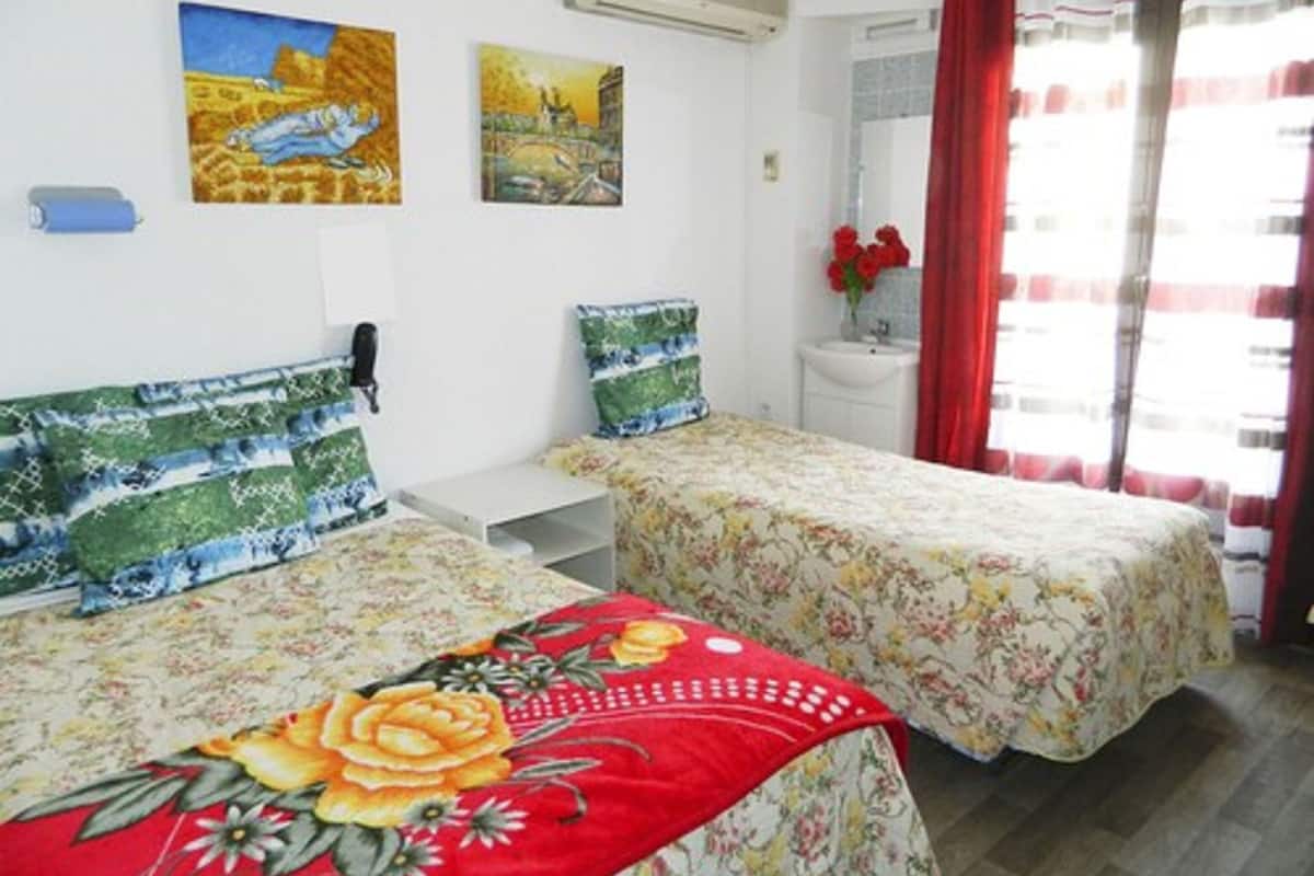 Una habitación con dos camas, cada una con ropa de cama floral, una mesita, un teléfono y dos cuadros en la pared.