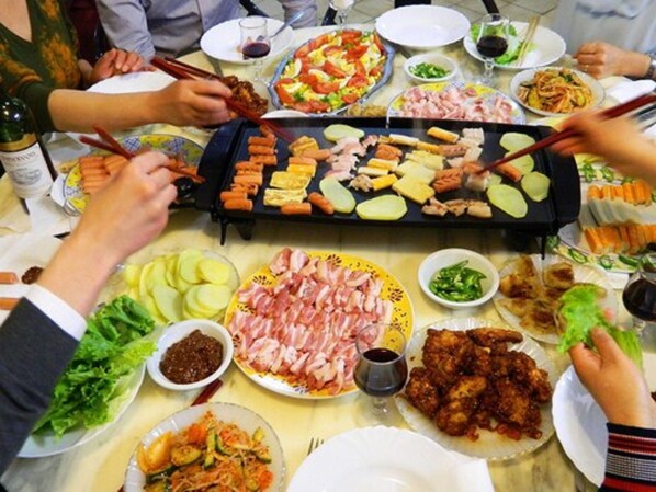 Une table à manger dressée avec divers plats, notamment des viandes grillées, des légumes et un plat chaud garni de brochettes.
