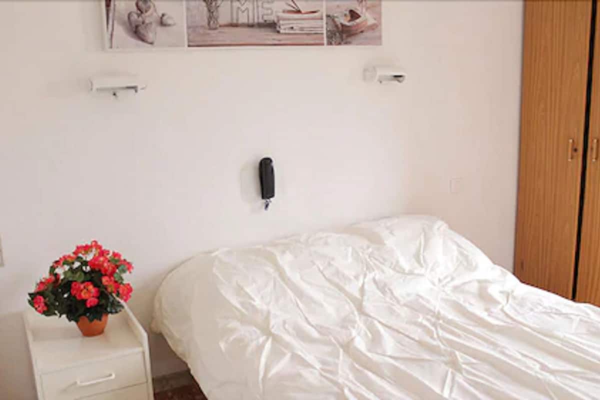 Un dormitorio con cama, mesita de noche con planta en maceta, teléfono de pared y armario de madera.