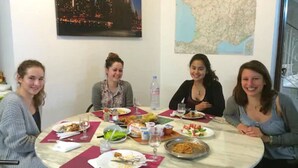 Un tavolo rotondo con quattro persone sedute, piatti di cibo e una mappa appesa al muro.