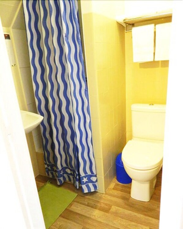 A small bathroom with a white toilet, a blue and white striped shower curtain, and a green rug on the floor. - Hotel Paris Star (Villejuif)