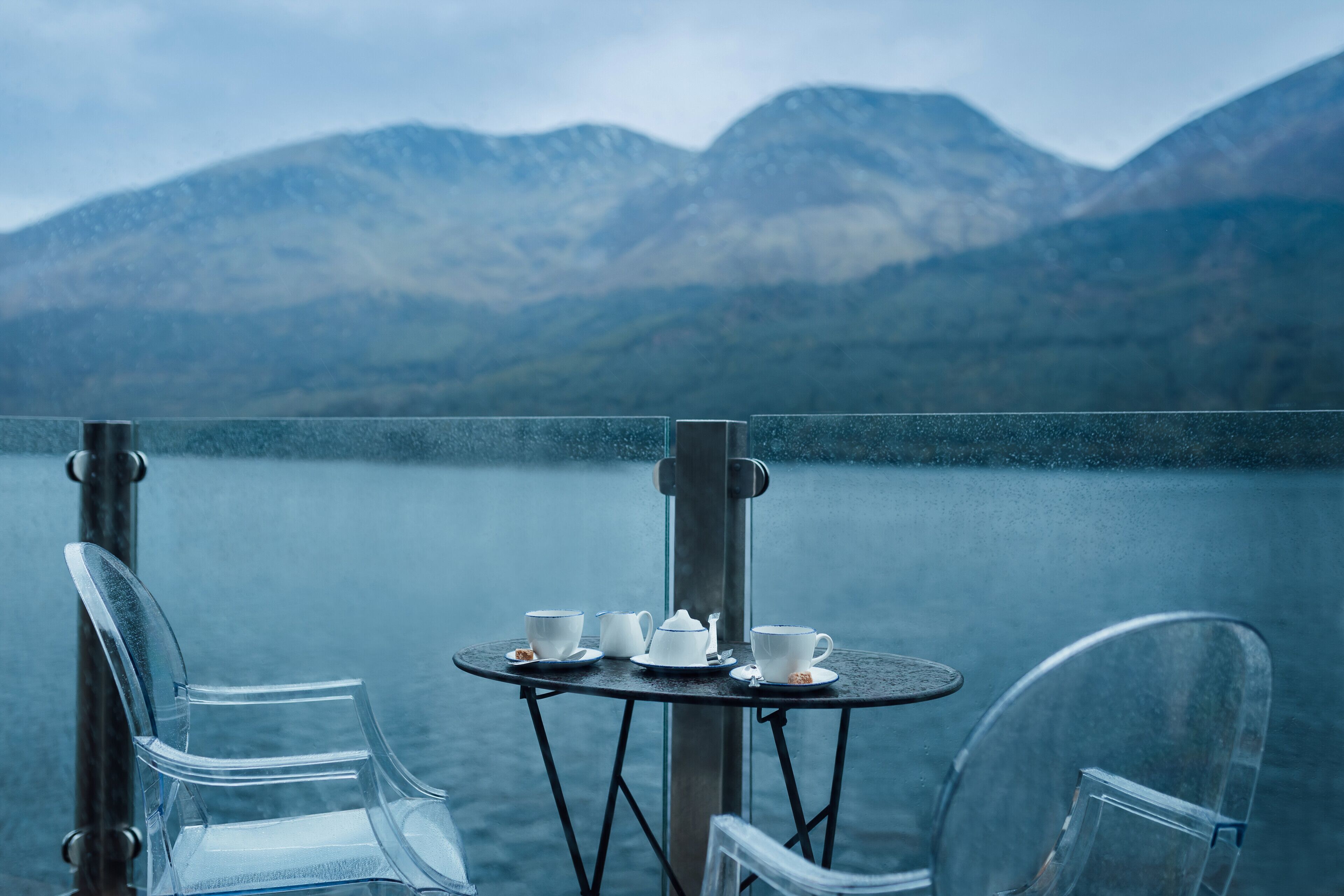 Une table en verre transparent offrant une vue sur les montagnes et un lac.