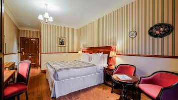 A hotel room with a bed, two chairs, a table, and a nightstand with a lamp.