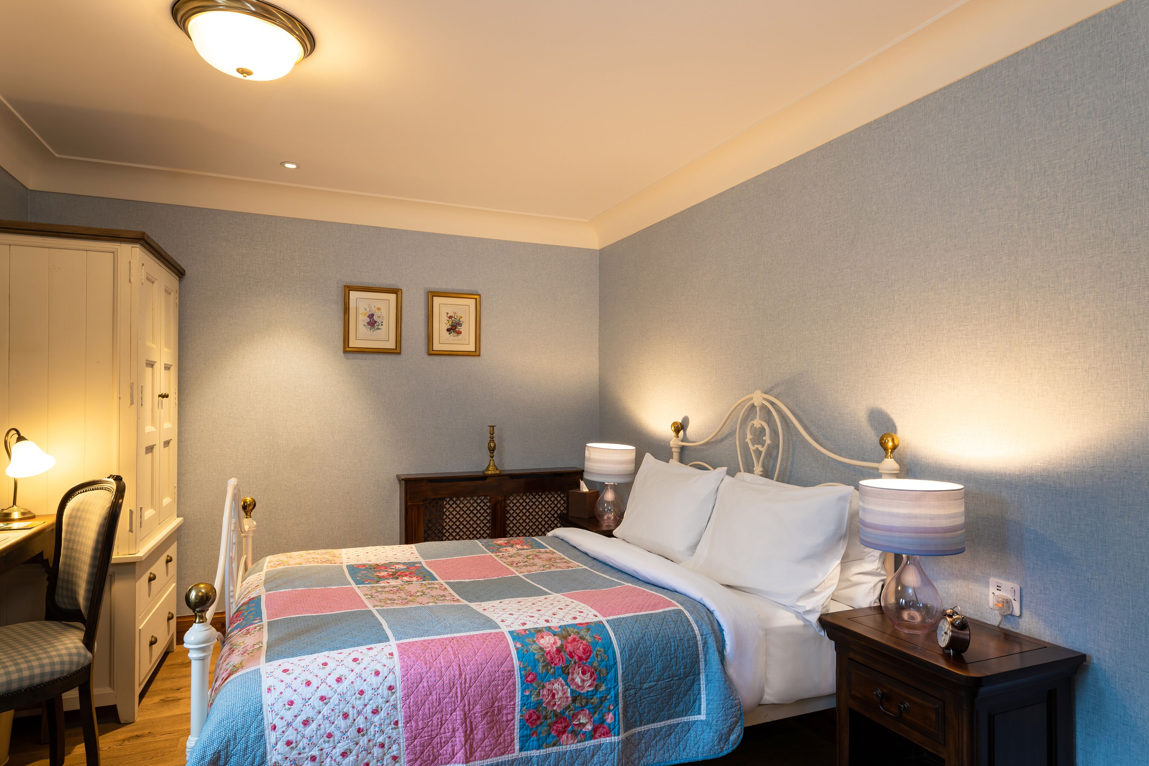 A neatly arranged bedroom with a bed, bedside lamps, a chair, a nightstand, and a wardrobe.
