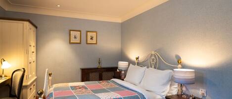A neatly arranged bedroom with a bed, bedside lamps, a chair, a nightstand, and a wardrobe.