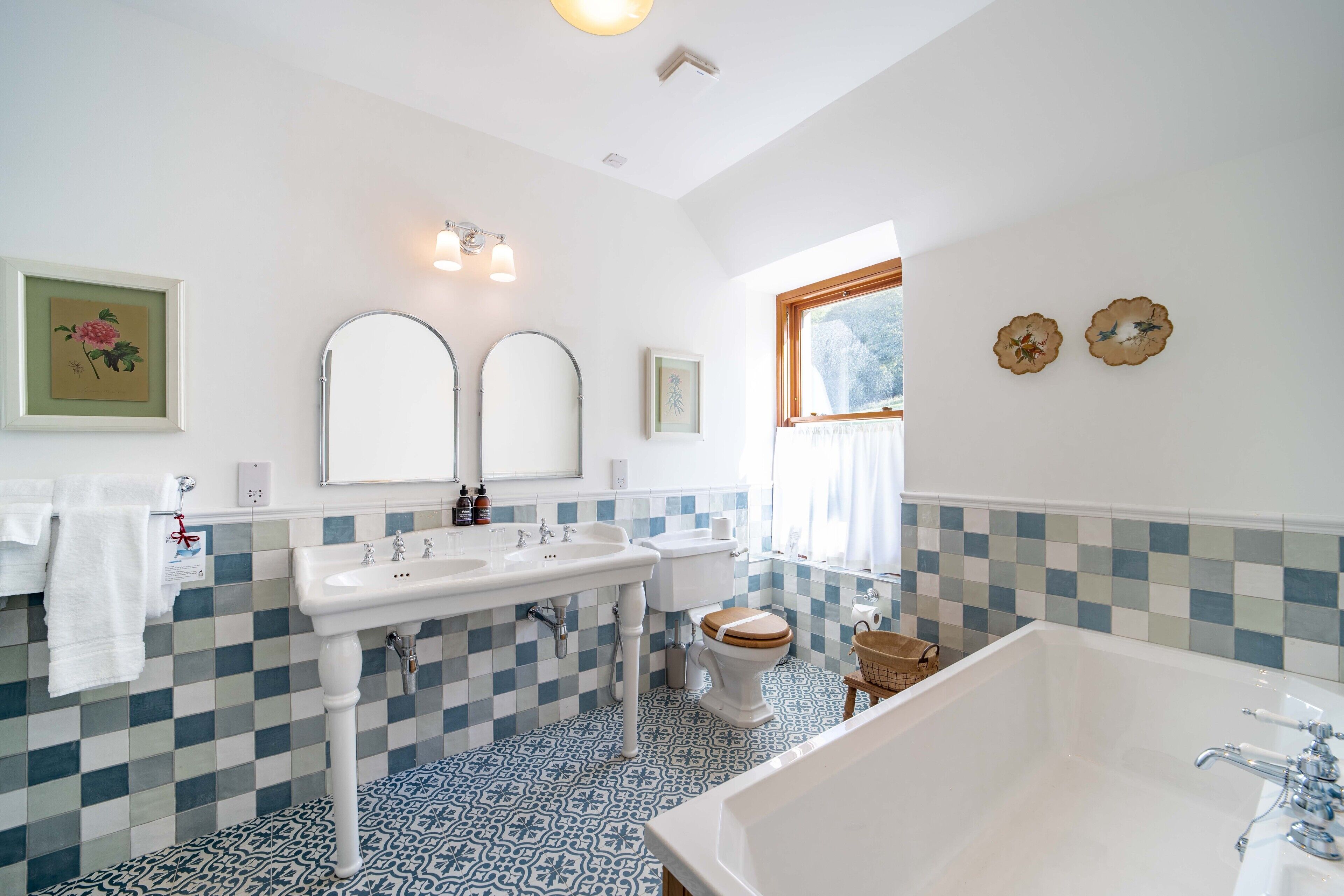 Ein Badezimmer mit Schachbrettfußboden, einem weißen Waschbecken, zwei Spiegeln, einer Toilette und einer Badewanne.