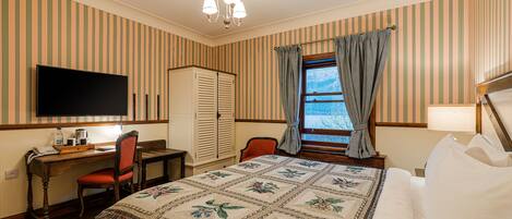 A hotel room with a bed, a desk with a chair, a television, a wardrobe, and a window with curtains.