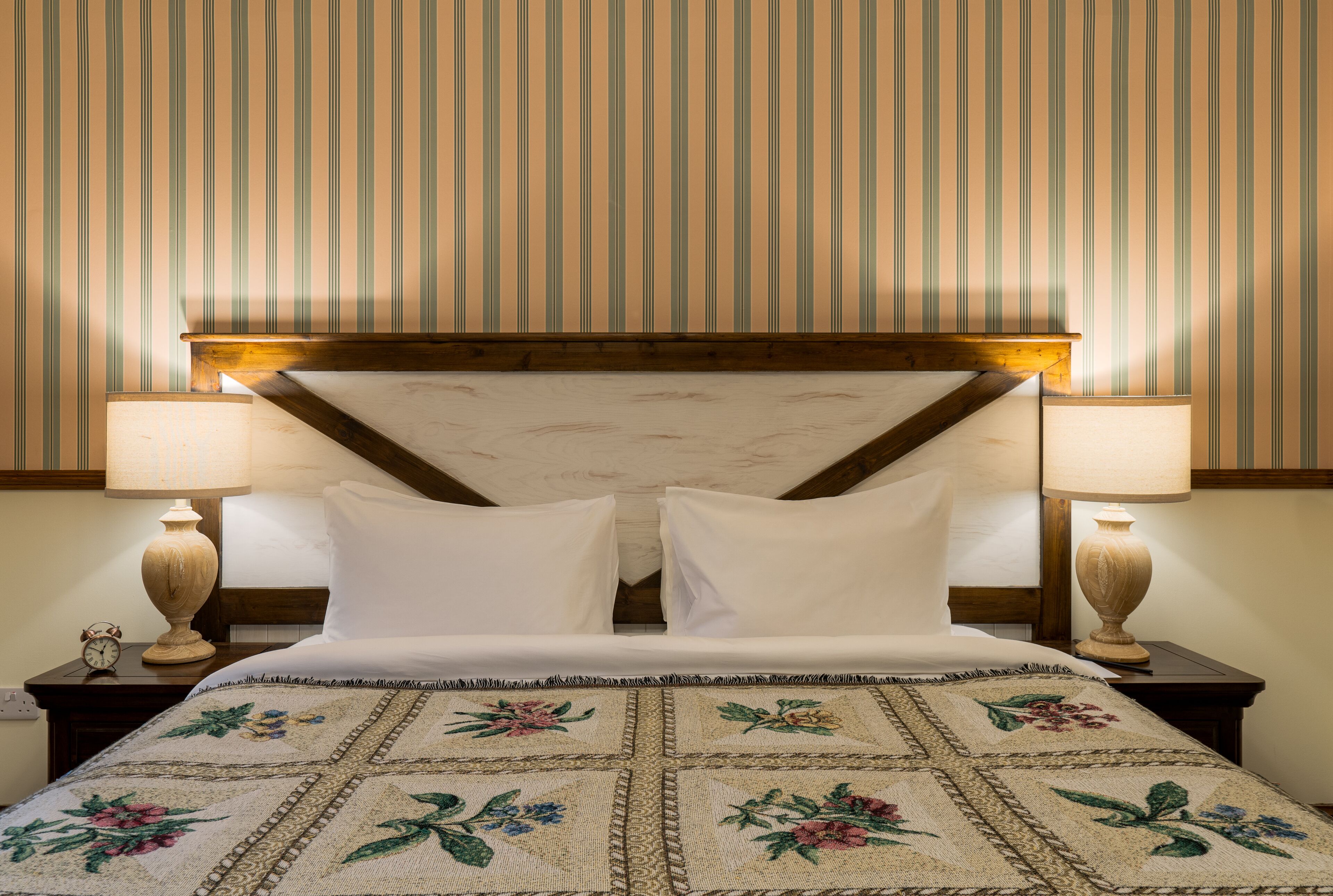 A neatly made bed with white linens, two bedside lamps, and a floral-patterned quilt.