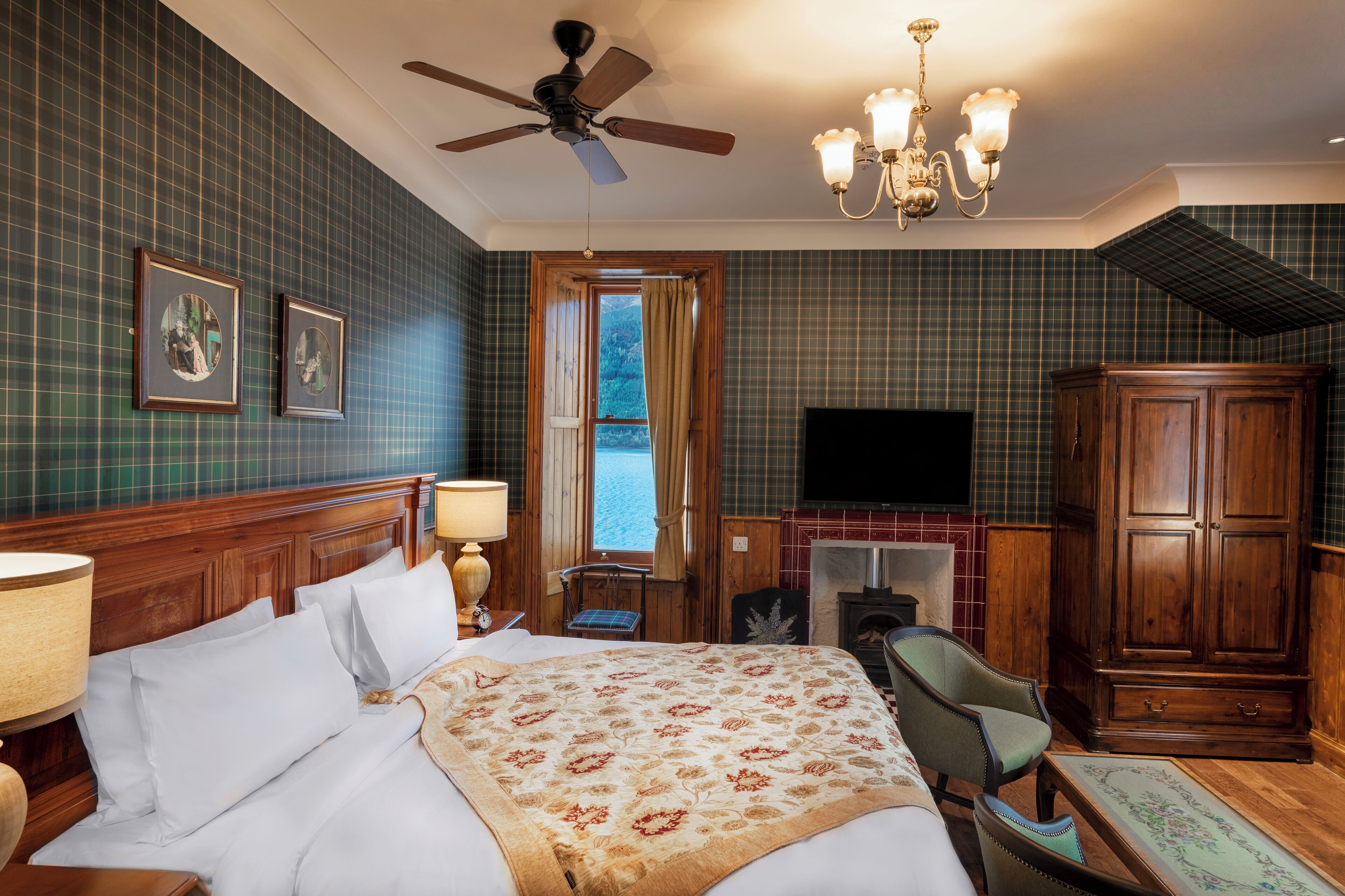 A hotel room with a bed, a desk, a chair, a television, a wardrobe, and a fireplace.