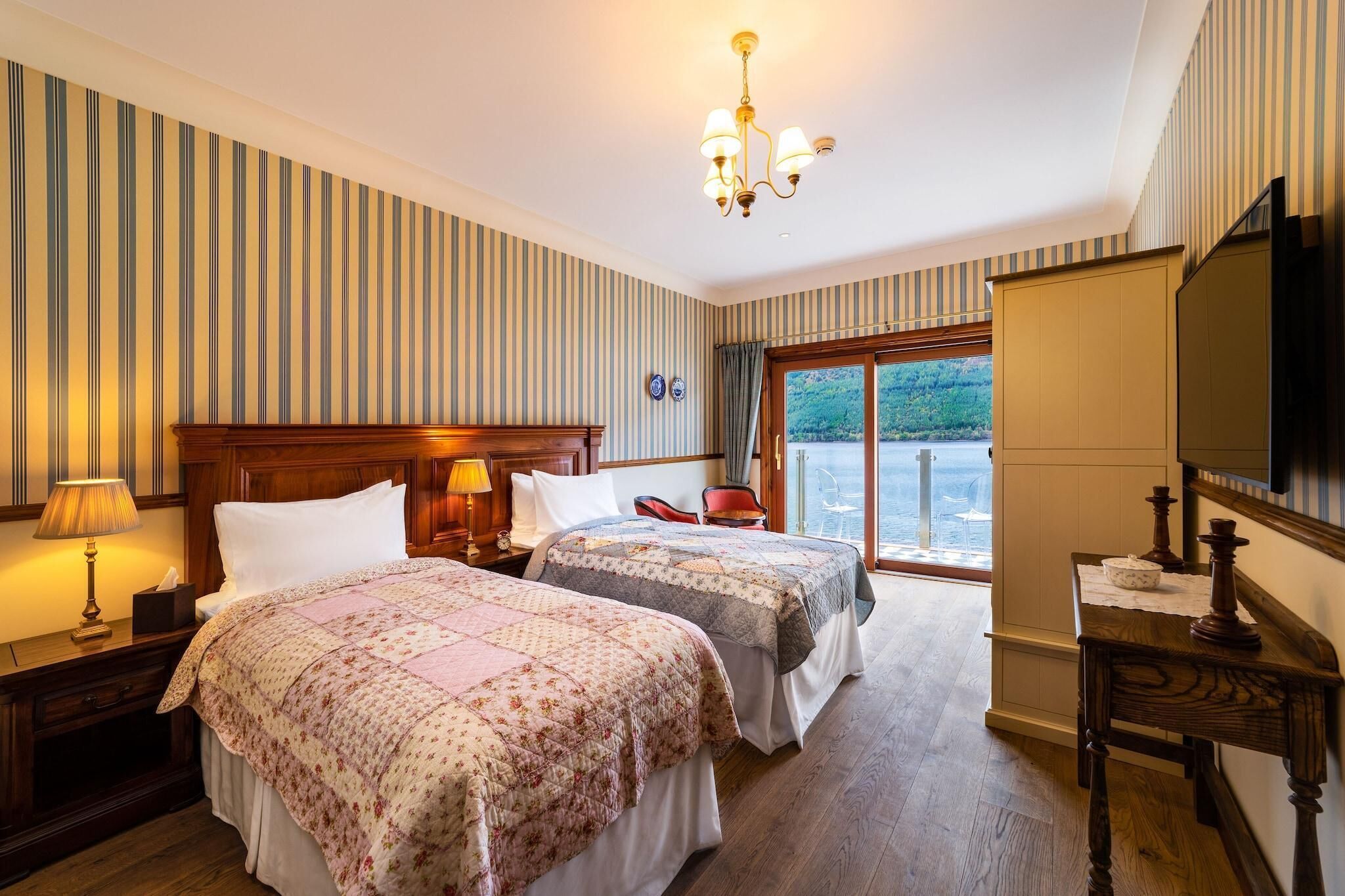 Une chambre d’hôtel avec deux lits, une tête de lit en bois, un lustre, une télévision et une vue sur l’extérieur.