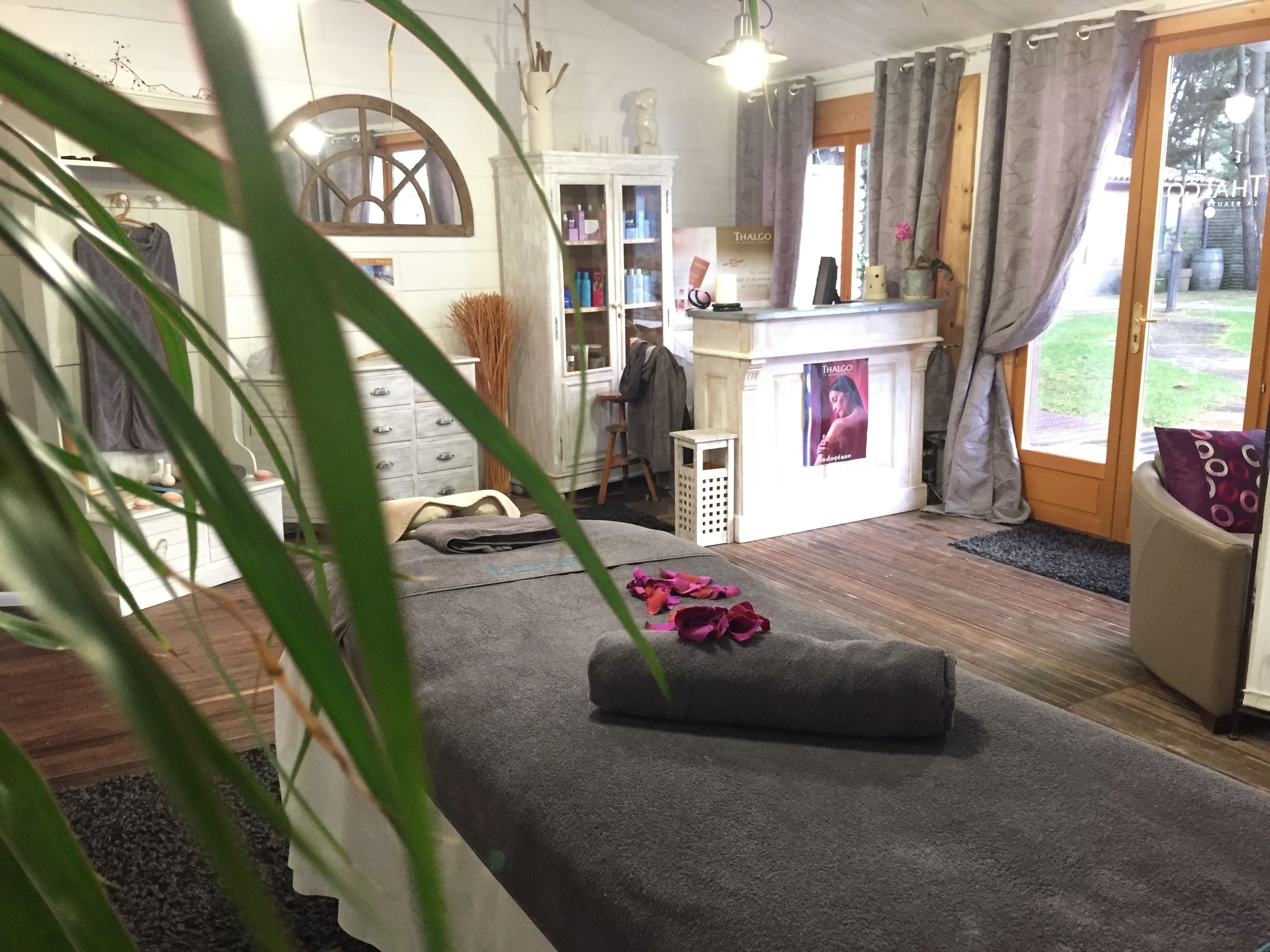 A room with a massage table, a small cabinet, a shelf with products, and a view of the outdoors.