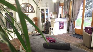 A room with a massage table, a small cabinet, a shelf with products, and a view of the outdoors.
