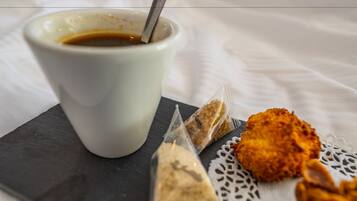 Une tasse blanche avec une cuillère, un morceau de nourriture frit et un petit paquet posés sur une planche d’ardoise.