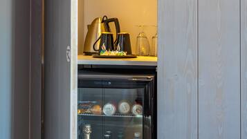 A minibar with a refrigerator, a coffee maker, and various bottles.