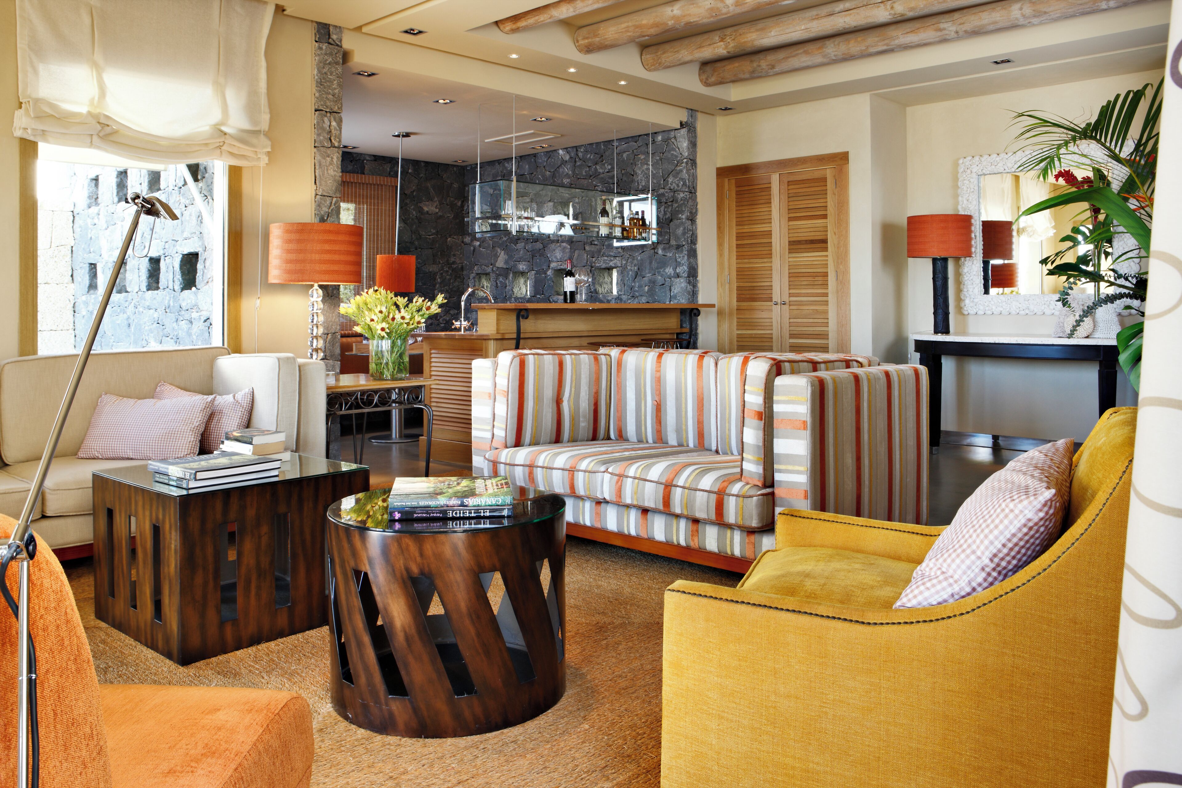 Ein modernes Wohnzimmer mit Sofa, Sessel und Couchtisch. Es gibt eine Küchenzeile mit Steinrückwand und Holzausbau.