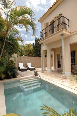 A swimming pool with lounge chairs, a balcony with a railing, and palm trees. - The Villas at Bahia del Duque (Adeje)
