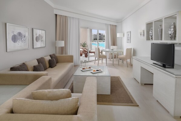 Habitación de hotel moderna con sofá, mesa de centro, televisión y balcón con vista a la piscina.