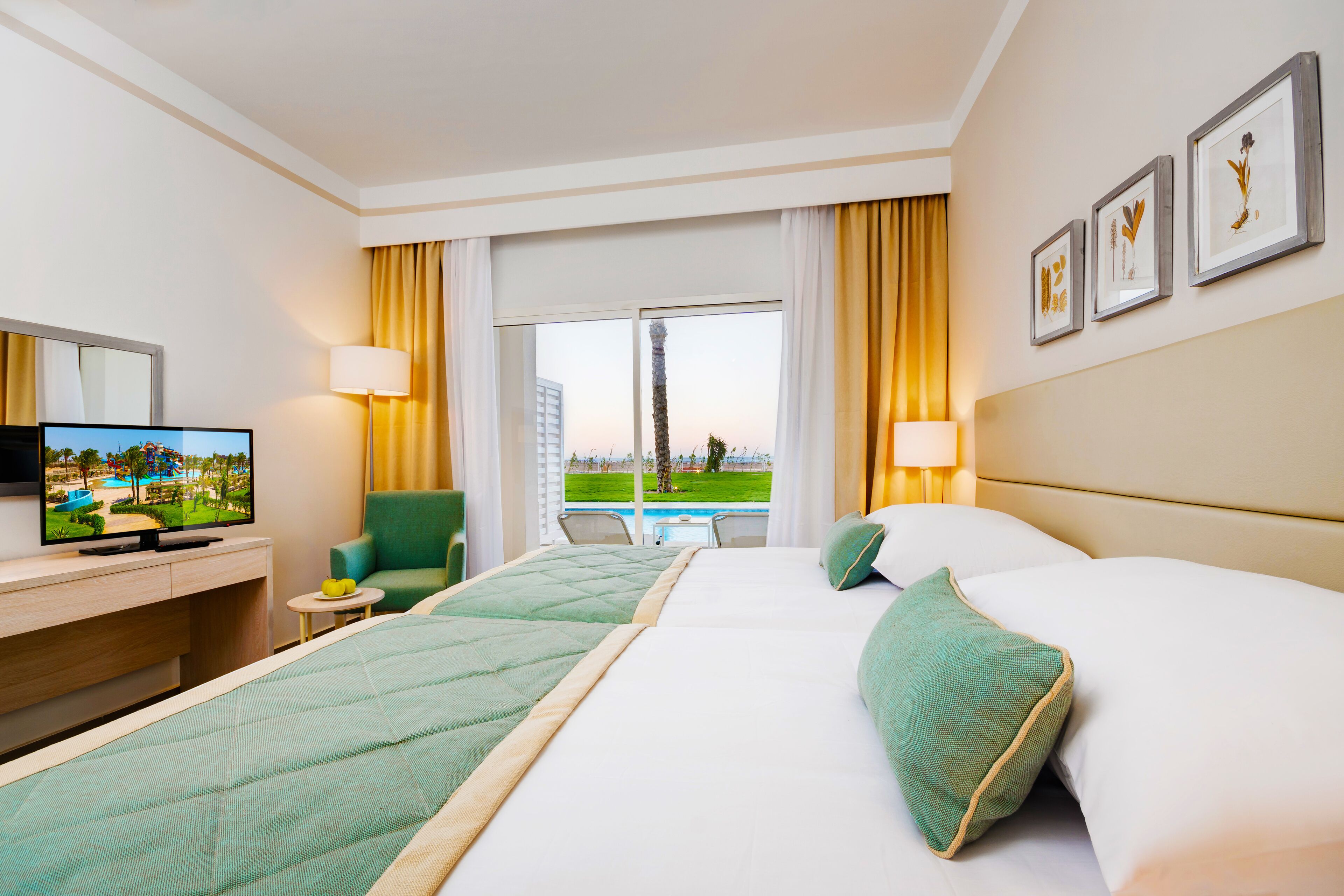 Een hotelkamer met twee bedden, een televisie, een bureau en uitzicht op een zwembad en groen.