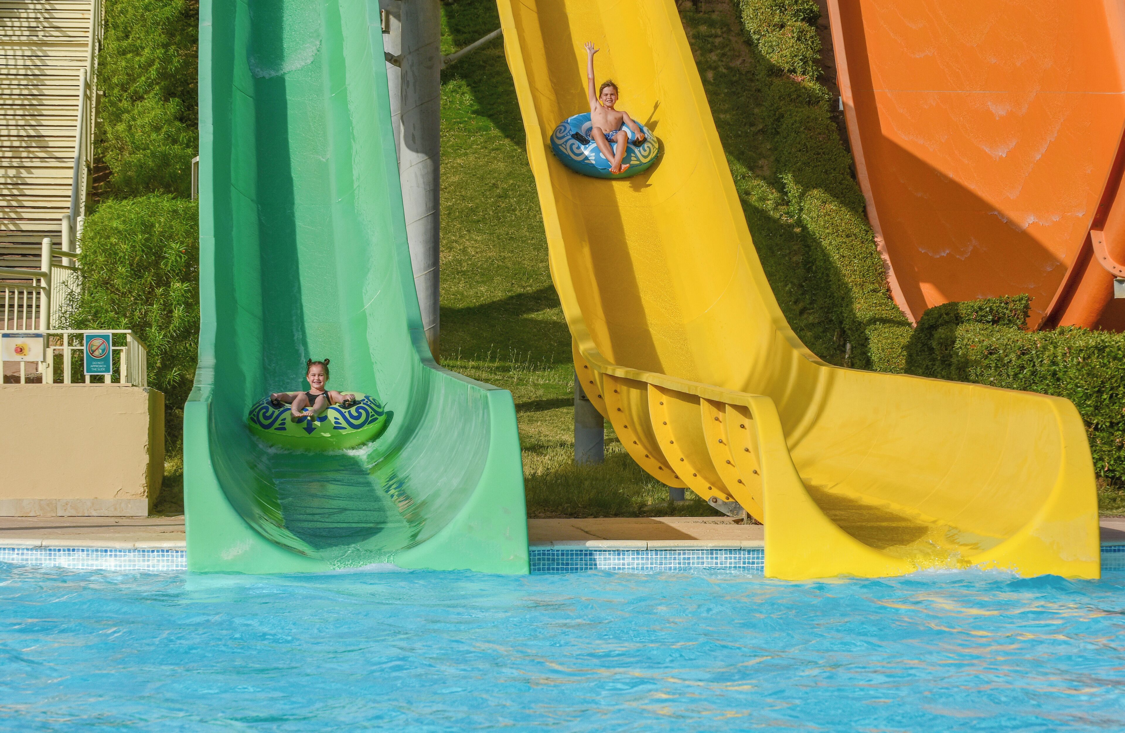 A water park with two slides, one green and one yellow, and a pool at the bottom.