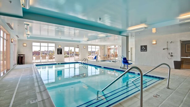 Una piscina interna con acqua cristallina, un sollevatore per piscina e vista sull'esterno tramite ampie finestre.