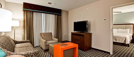 Habitación de hotel con sofá, sillón, una mesita, televisión y cama.