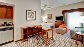 Habitación de hotel con kitchenette, una cama, un escritorio con silla, televisión y alfombra estampada.
