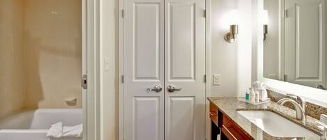 A bathroom with a double door, a bathtub, a sink with a granite countertop, and a mirror above the sink.