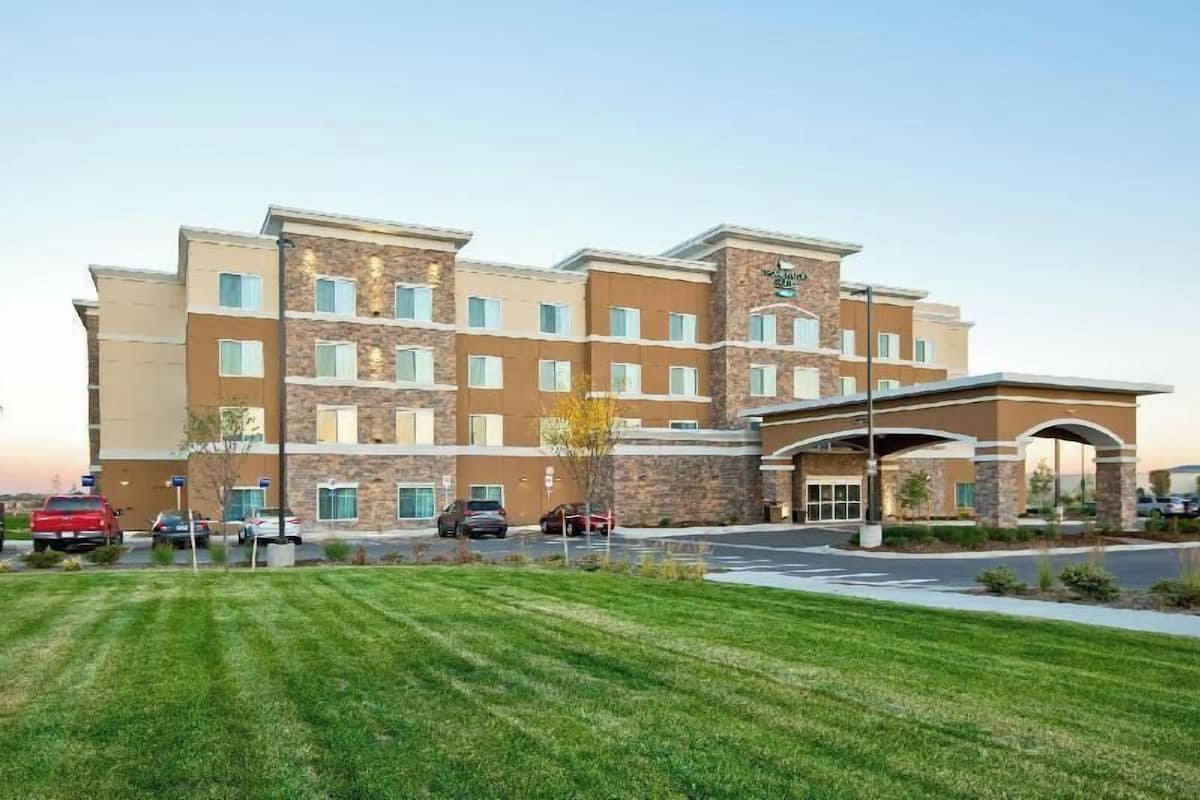 A multi-story hotel with a stone facade, a covered entrance, and a parking lot with several cars.