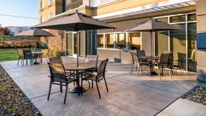 An outdoor patio with tables and chairs, large umbrellas, and a stone wall. - Hampton Inn Kennewick at Southridge (Kennewick)