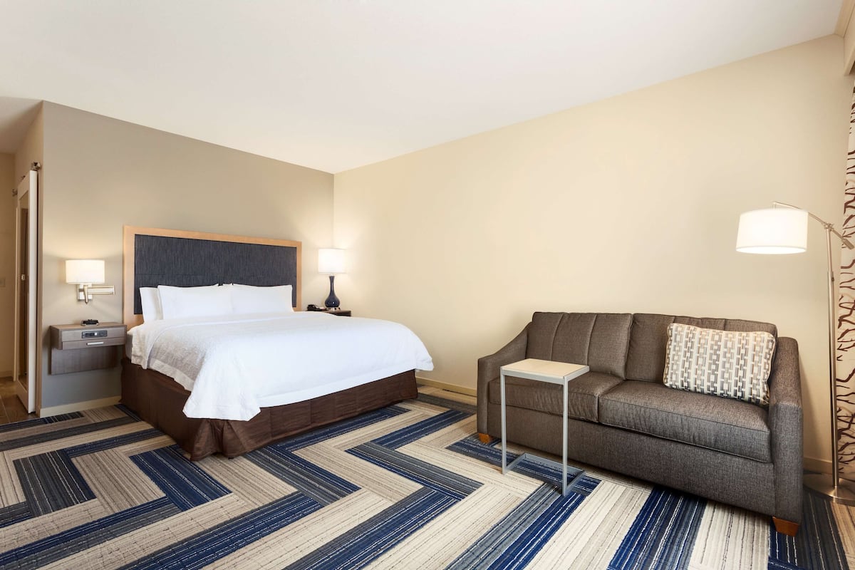 A hotel room with a large bed, a sofa, a small table, and a nightstand.