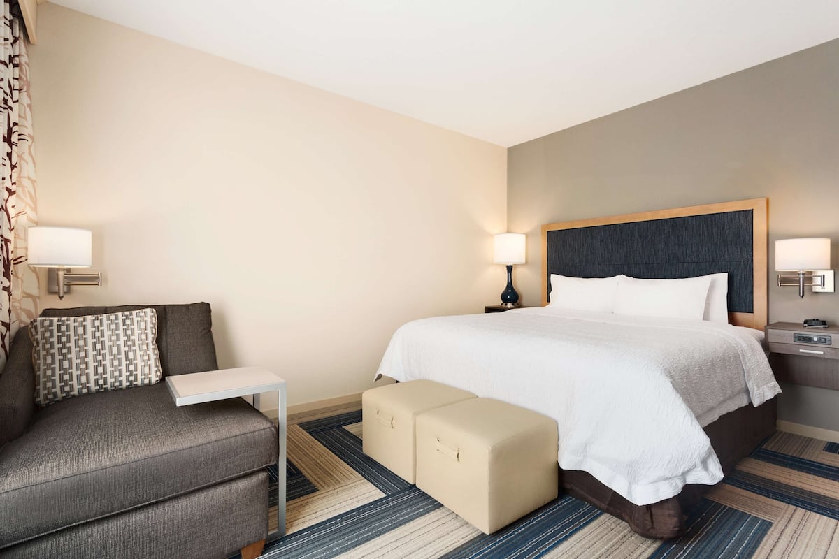 A hotel room with a bed, a sofa, a small table, and a nightstand with lamps.