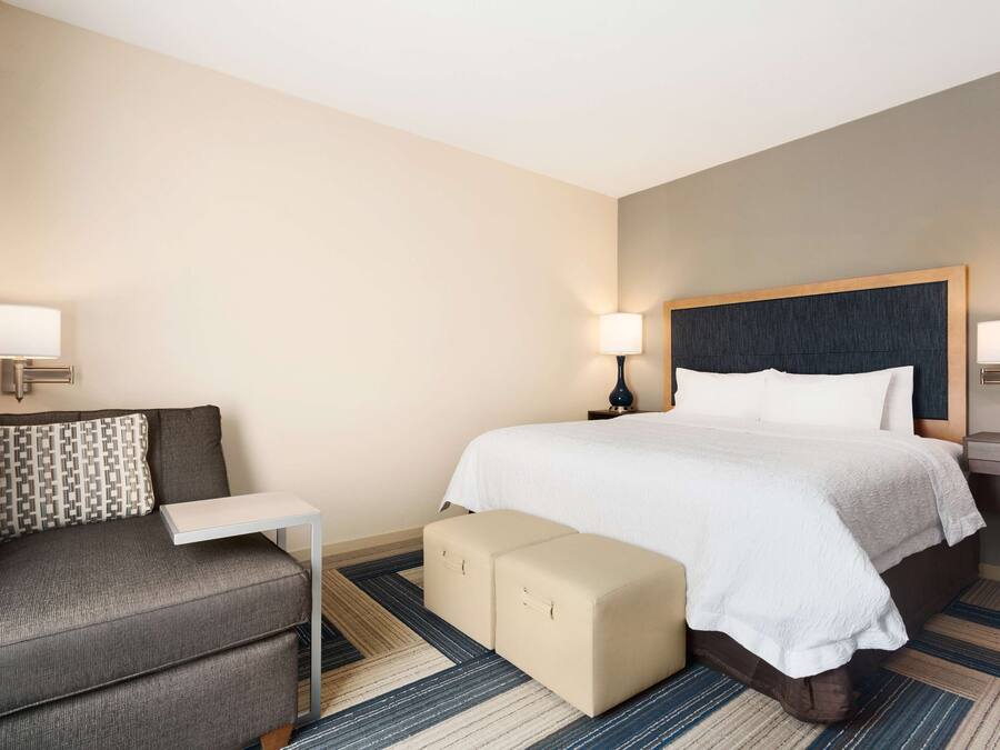 A hotel room with a bed, a sofa, a small table, and a nightstand with lamps.