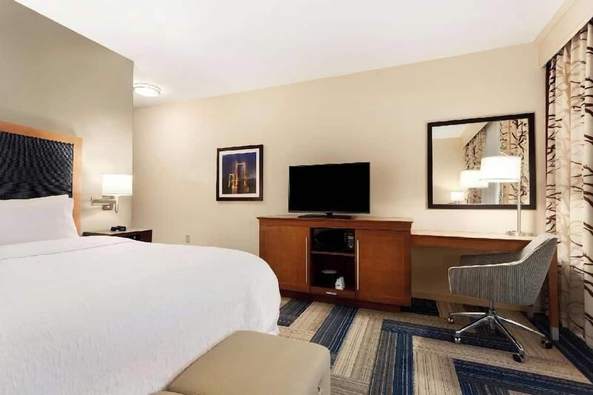 A hotel room with a bed, a desk with a television, a chair, and a mirror.