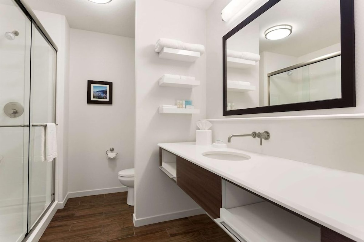 A modern bathroom with a glass shower enclosure, white vanity with a large mirror, and a wooden cabinet.