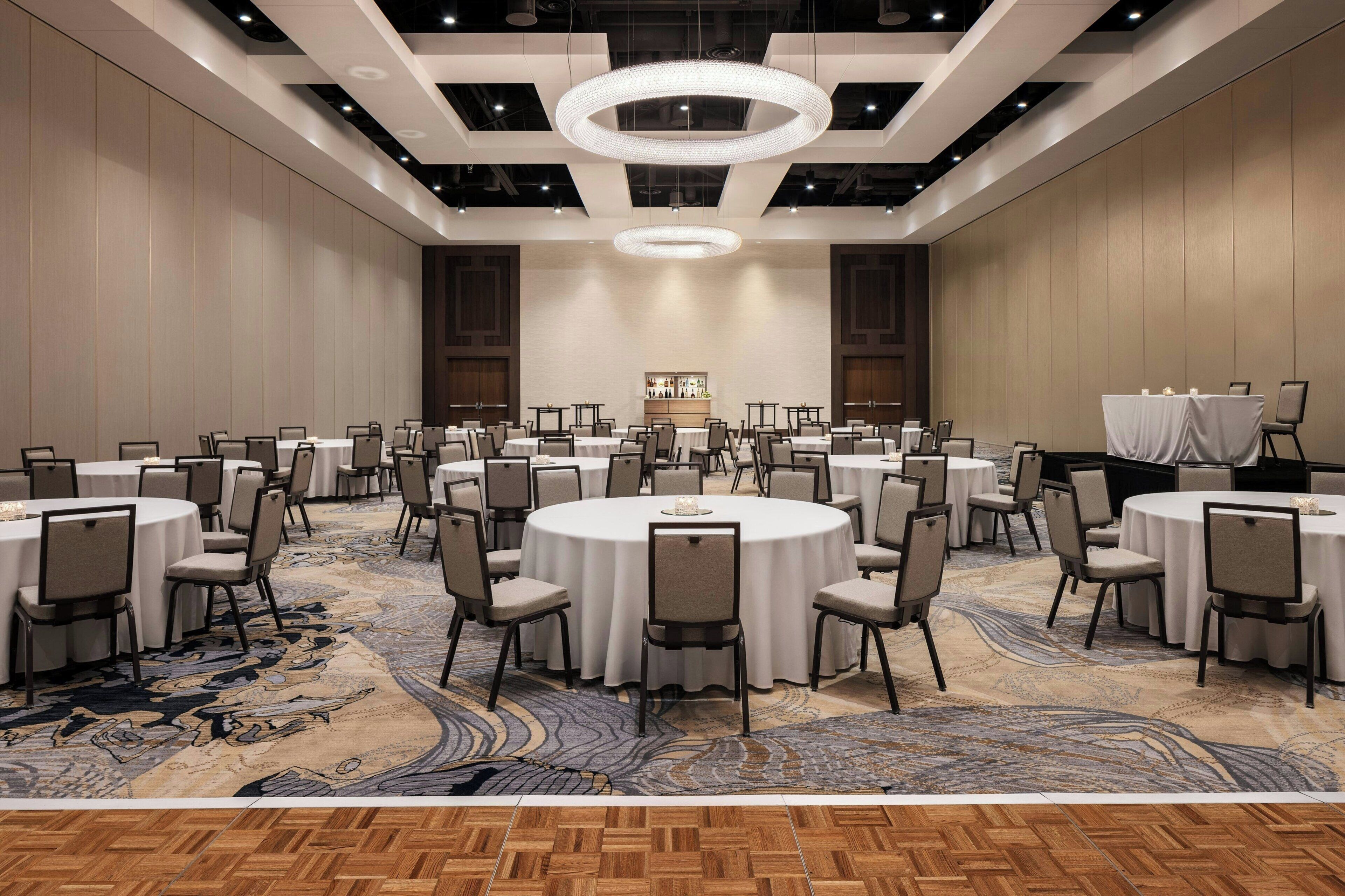 A large conference room with multiple round tables, chairs, and a patterned carpet.
