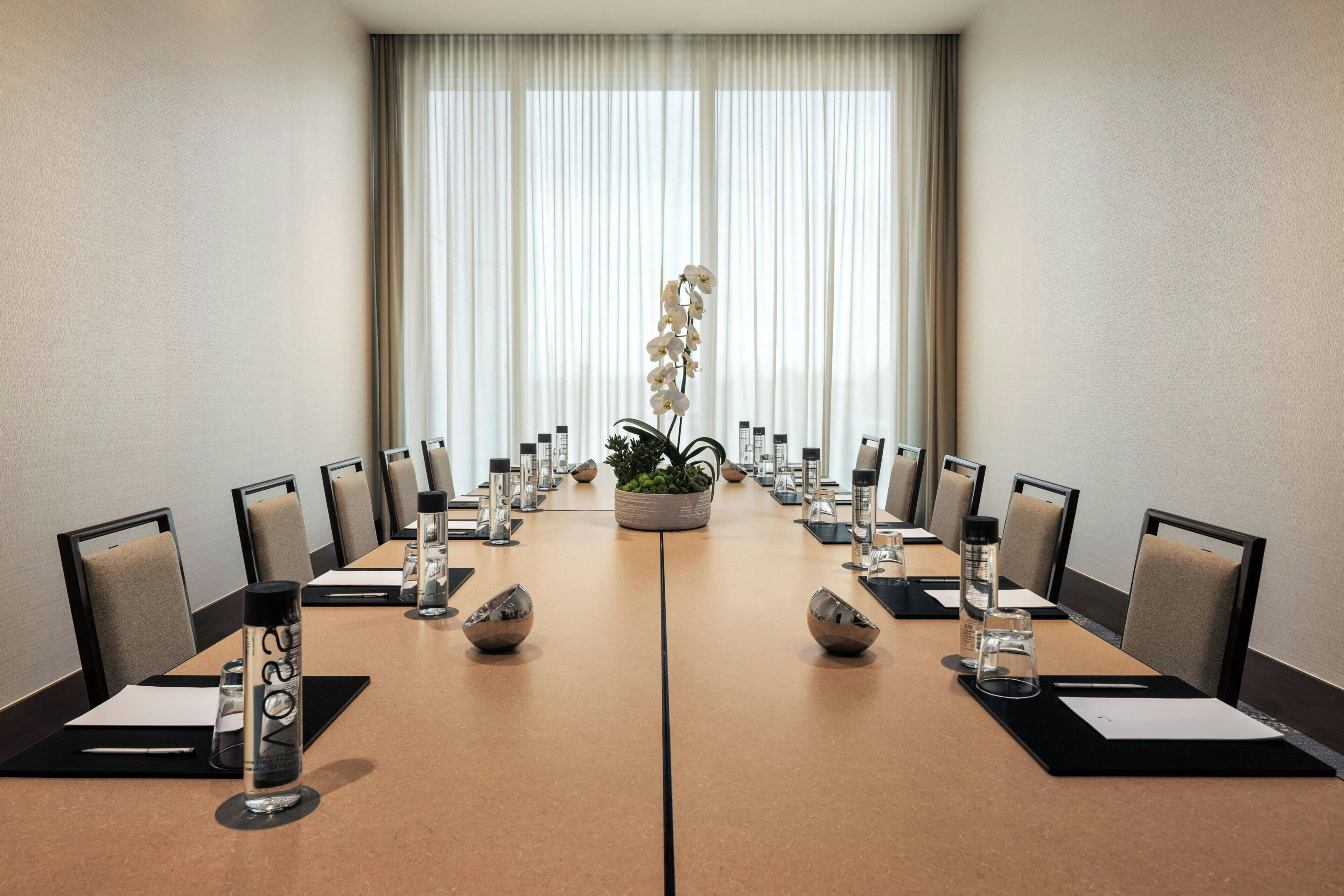 A conference room with a long table, chairs, a potted plant, and water bottles.