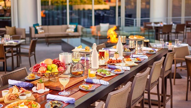 Una larga mesa de comedor dispuesta con diversos platos, bebidas y una chimenea de fondo.