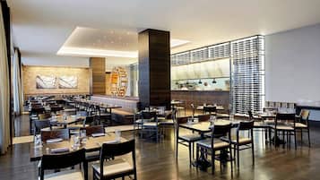 A spacious restaurant with multiple dining tables and chairs, a bar area, and a modern interior design.